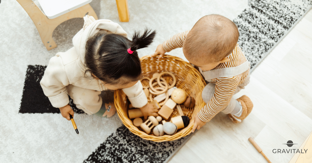 Két kisgyermek egy puha szőnyegen ül, és közösen játszik természetes fa Montessori-játékokkal egy napfényes, minimalista gyerekszobában.