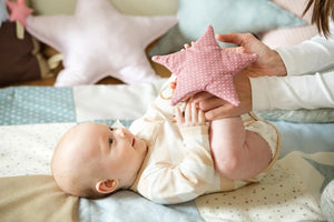 Bebé tumbado sobre manta de patchwork de guardería sosteniendo almohada de estrella rosa de lunares.