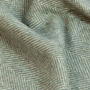 Dettaglio ravvicinato della trama di una morbida coperta in lana di alpaca naturale a spina di pesce verde chiaro e bianco