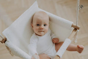 Baby in white plush hammock swing with wooden frame, cozy nursery decor