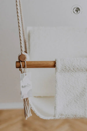 White fluffy baby hammock with wooden bar and rope, Noft Kids tag visible, nursery decor
