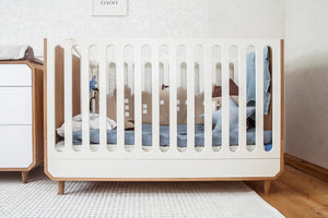 Modern wooden baby crib with white slats, blue bedding, and decorative cushions in a nursery