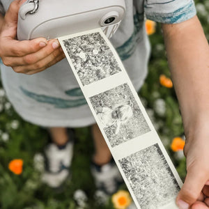 Child holding instant camera with black and white photo strip in garden
