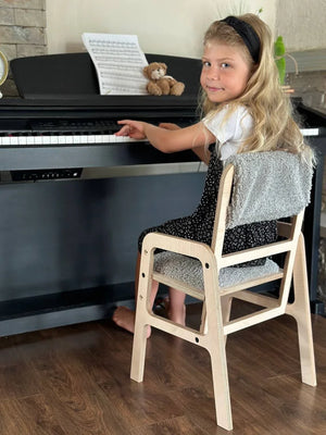 Child on natural wood piano chair with gray cushion, playing black digital piano