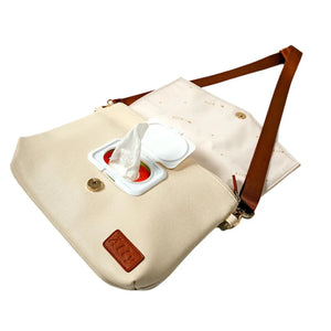 Schräge Ansicht der offenen hellcremefarbenen Älly Cappuccino Wickeltasche: ein Feuchttuch wird aus dem praktischen integrierten Spender gezogen.