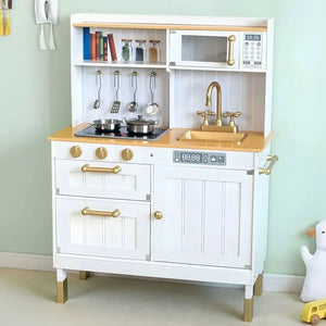 Photo lifestyle de la grande cuisine interactive en bois Angelove dans une chambre d'enfant moderne, mettant en valeur son design blanc, ses accents dorés, ses plaques LED et ses ustensiles en métal suspendus.