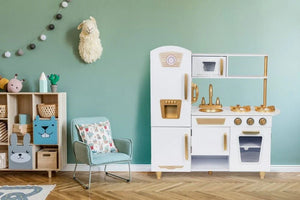 La grande cuisine jouet Angelove blanche et dorée joliment mise en scène dans une salle de jeux moderne avec murs vert menthe et parquet à chevrons.