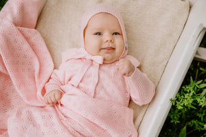 Bébé fille enveloppée dans une couverture et un bonnet en tricot rose coton bio avec motif délicat