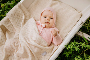 Bébé dans un berceau portant un tricot pointelle rose avec couverture assortie