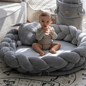 Graues, geflochtenes Nestchen-Spielkissen mit weicher Cord-Umrandung, Baby sitzt darin