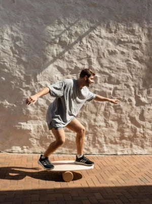 Hombre manteniendo el equilibrio sobre una tabla de equilibrio de madera con rodillo cilíndrico en pavimento de ladrillo