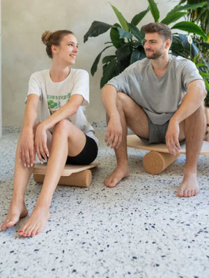 Dos personas usando tablas de equilibrio de madera con rodillos de ejercicio cilíndricos en un entorno interior moderno