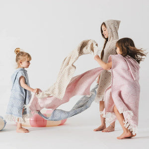 Enfants portant des ponchos de bain en bambou à capuche, rose pastel, bleu et beige, motifs vagues et franges