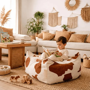 Enfant lisant un livre sur un pouf à motif vache dans un salon cosy.