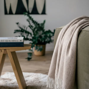 Coperta in lana di alpaca naturale a spina di pesce beige appoggiata su un divano verde in un soggiorno accogliente e moderno