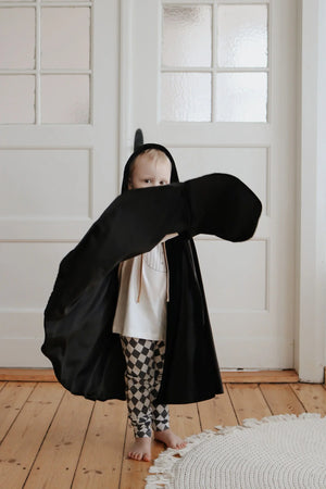 Child wearing hooded black Moi Mili cape indoors with cape spread during movement