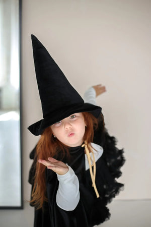 Child in black Moi Mili cape and tall witch hat blowing a kiss during dress-up play