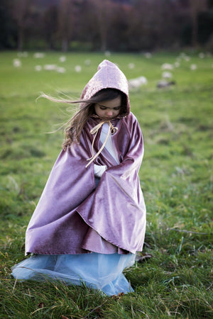 Child looking down while wearing the flowing Cosmic Pearl hooded cape in a grassy field