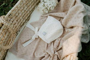 Cream knit baby bonnet and beige patterned blanket in woven basket