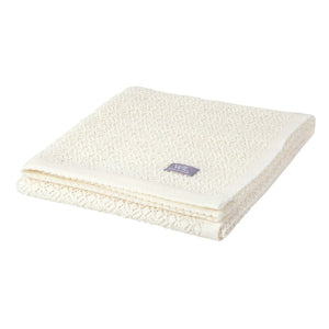 Couverture bébé en tricot crème avec motif losanges texturé et étiquette, pliée sur fond blanc