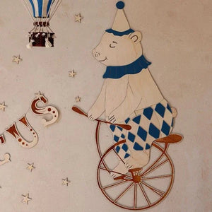 Wandbild aus Holz: Bär auf dem Einrad mit blau-karierter Hose, Partyhut und Heißluftballon-Deko
