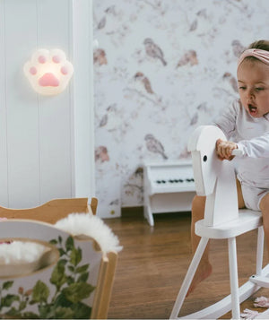 Nursery con bambino su cavallo a dondolo bianco, luce notturna a zampetta rosa sulla parete, carta da parati con uccellini e cesto giocattoli floreale