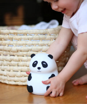 Bébé jouant avec une veilleuse panda en silicone noir et blanc à côté d'un panier en osier