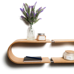 Mensola fluttuante da parete ovale con finitura in legno chiaro, decorata con fiori in vaso di vetro, candele e taccuini