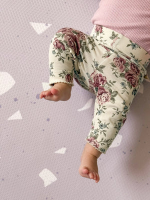 Tapis de jeu puzzle en mousse lavande à motif terrazzo sous un bébé en pantalon fleuri