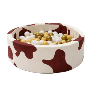Foam round ball pit with cow print pattern, filled with white, gold, and yellow balls