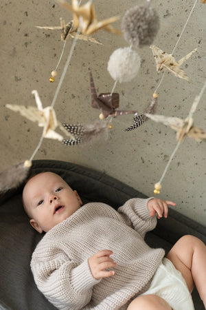 Close-up of a baby beneath the moving origami cranes, feathers and pompoms