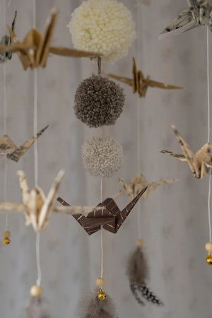 Close-up of cream, grey and brown yarn pompoms with folded paper cranes