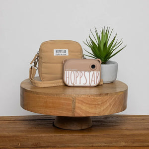 Appareil photo enfant Hoppstar beige et étui matelassé sur support en bois avec plante en pot