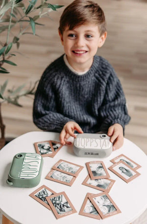 Enfant jouant au jeu de mémoire Hoppstar avec appareils photo pastel et cartes photo sur table blanche