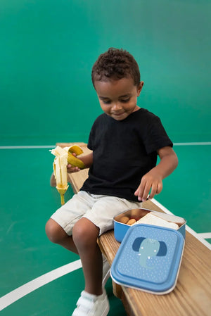 Grande lunchbox bleue avec design éléphant, contenant un en-cas, enfant mangeant à côté.