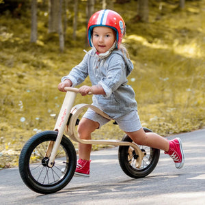 Child riding wooden balance bike with black tires and 'leg&go' branding, wearing red helmet outdoors