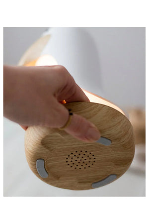 Mano sosteniendo una lámpara infantil con base de madera, altavoz integrado e iluminación suave