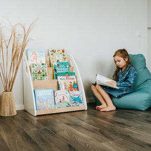 Child reading on a teal beanbag beside a four-level Montessori bookshelf filled with picture books
