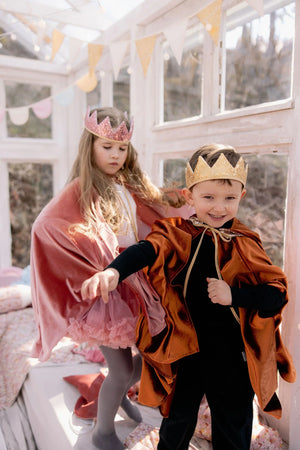 Children in pink and ginger magic capes and crowns during imaginative dress-up play