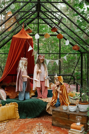 Children wearing pink and ginger fantasy capes with crowns and star wands in a greenhouse play setting