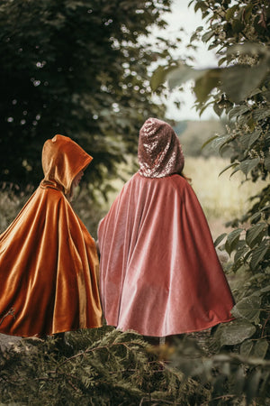 Back view of children wearing pink and ginger Moi Mili magic capes while exploring a woodland setting
