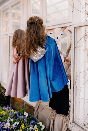 Back view of children wearing turquoise and pink Moi Mili capes with sparkling sequin hoods in a conservatory
