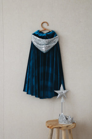 Moi Mili Snow Queen cape hanging on wall with silver-sequin hood, matching crown and star wand