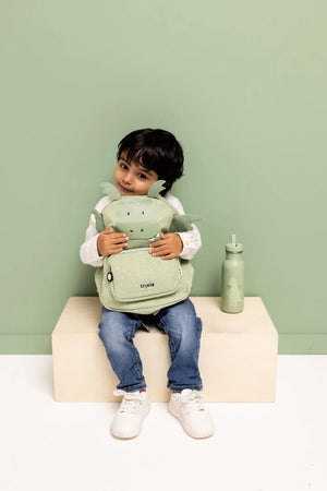 Child sitting and hugging the green Trixie Mr. Dragon backpack beside a matching bottle
