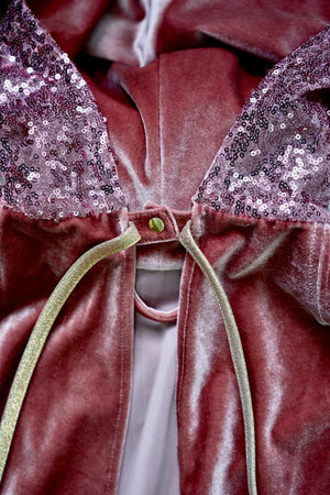 Close-up of Moi Mili Pink Riding Hood cape showing sequin hood, snap fastening and gold ties
