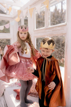 Children wearing pink and ginger Moi Mili capes with sparkling crowns in a bright playroom