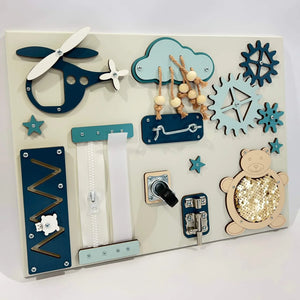 Wooden sensory activity board with blue and cream panels, zippers, gears, cloud with beads, and sequin bear for toddler development