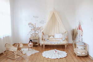 Wide children’s room with a raw cotton canopy above a rattan bed and carousel wall illustrations