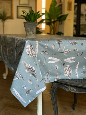 Blue tablecloth with botanical print featuring pinecones, dragonflies, and moths on dining table