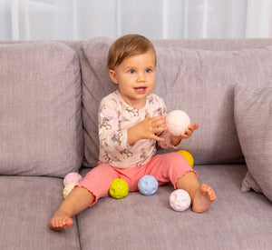Neonato seduto sul divano con set di palline sensoriali pastello, testurizzate per lo sviluppo tattile